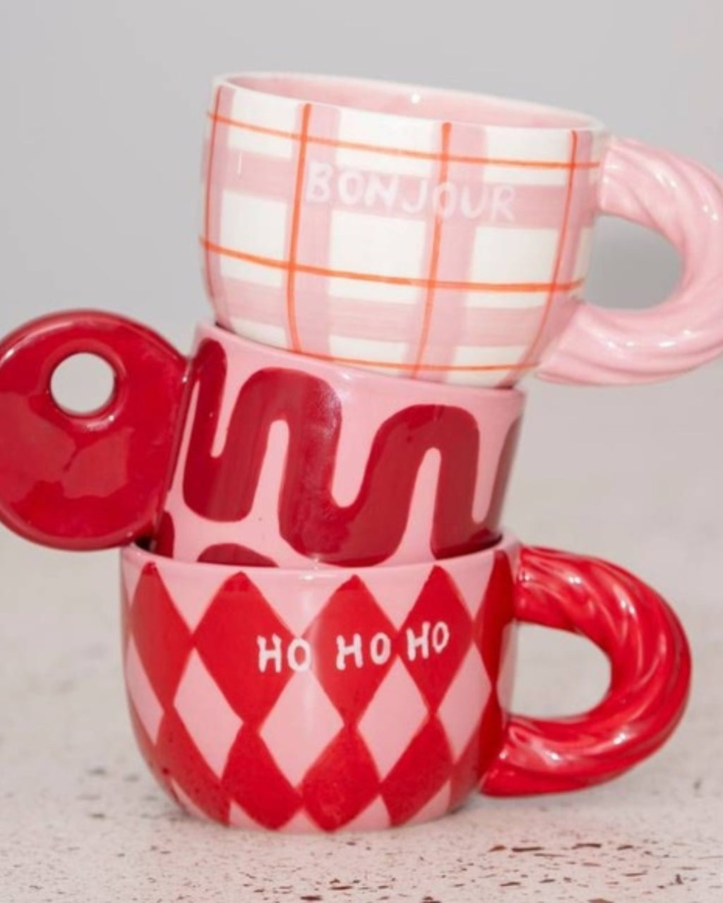 Χειροποίητη κεραμική κούπα Qué Rico Natalia με πολύχρωμο μοτίβο Harlequin σε κόκκινο και ροζ, και χαρακτηριστική στριφτή λαβή.