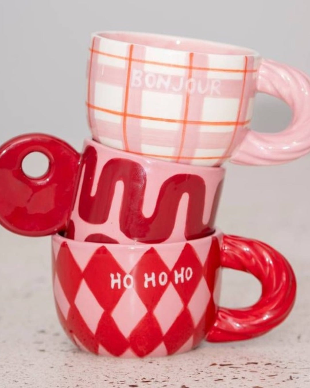 Χειροποίητη κεραμική κούπα Qué Rico Natalia με πολύχρωμο μοτίβο Harlequin σε κόκκινο και ροζ, και χαρακτηριστική στριφτή λαβή.